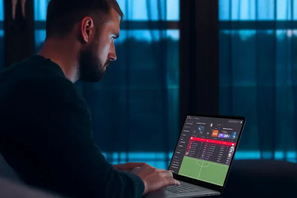 GOOB111 মোবাইল অ্যাপ — ক্যাসিনো ও স্পোর্টসের সম্পূর্ণ হাব একজন পুরুষ তার ল্যাপটপে মনোযোগ দিয়ে কাজ করছেন, ব্যাকগ্রাউন্ডে লাইভ স্ট্যাটস — যা GOOB111 মোবাইল অ্যাপের স্পোর্টস ও গেমিং ফিচারগুলোকে তুলে ধরে।