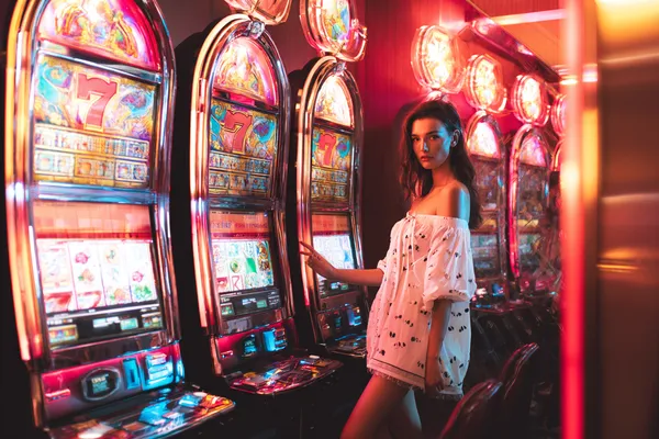GOOB111 Slots — Thousands of exciting themes and jackpots A stylish woman beside vibrant slot machines displaying glowing sevens, showcasing the variety of top slots at GOOB111.