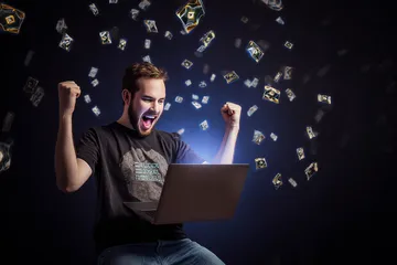 A man celebrating a winning moment on his laptop while gaming symbols float around him, capturing the excitement of GOOB111 games.